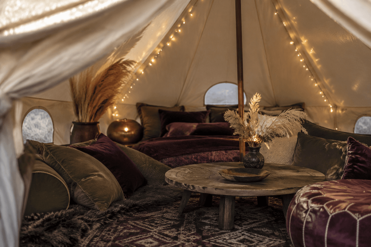 Boutique canvas bell tent interior styled with brass string lights, mulberry velvet cushions and a wool rug