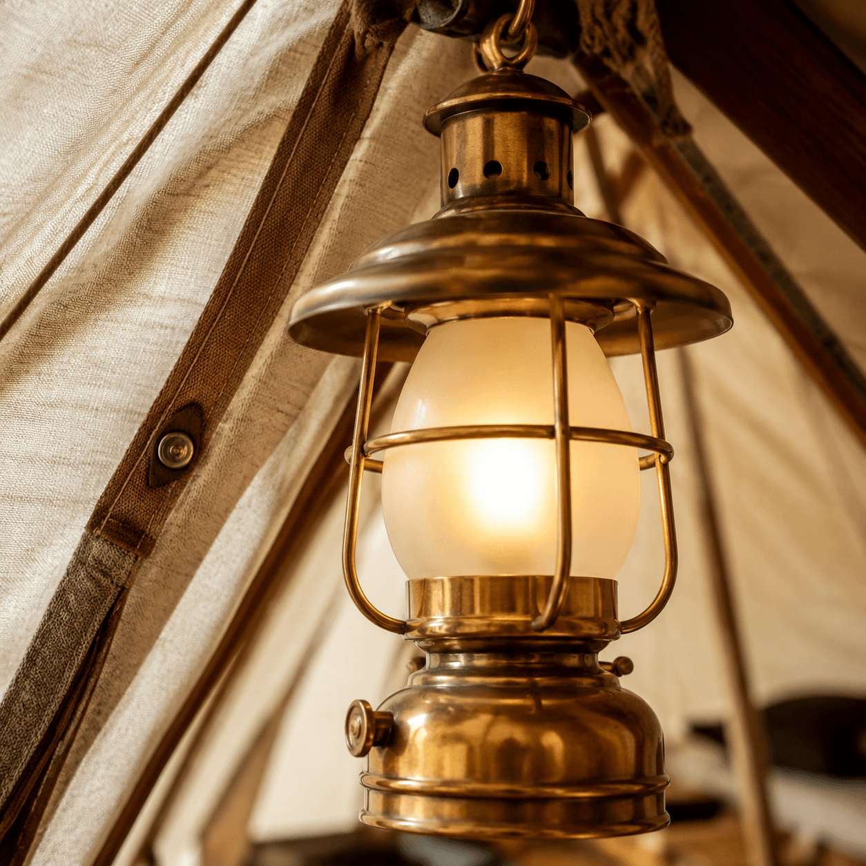 Close-up of an unlit brass lantern with frosted glass hanging inside a cream canvas tent